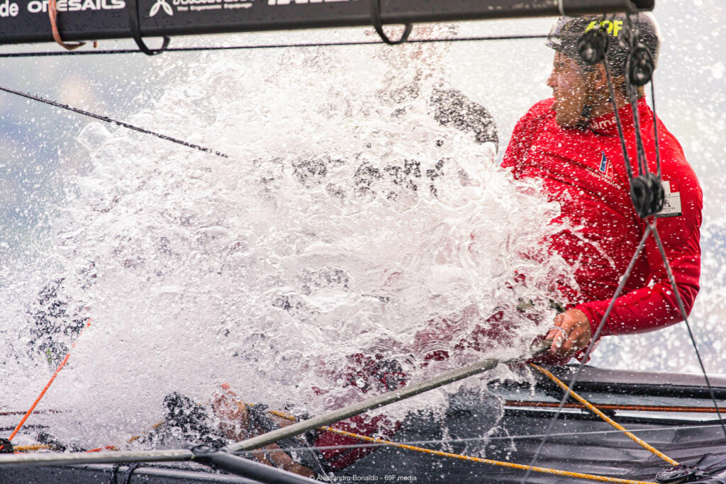 A skipper getting splashed by a wave as they sail upwind.