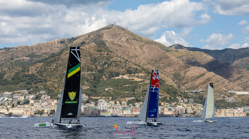 Trimarans sailing with a stunning backdrop of mountains.