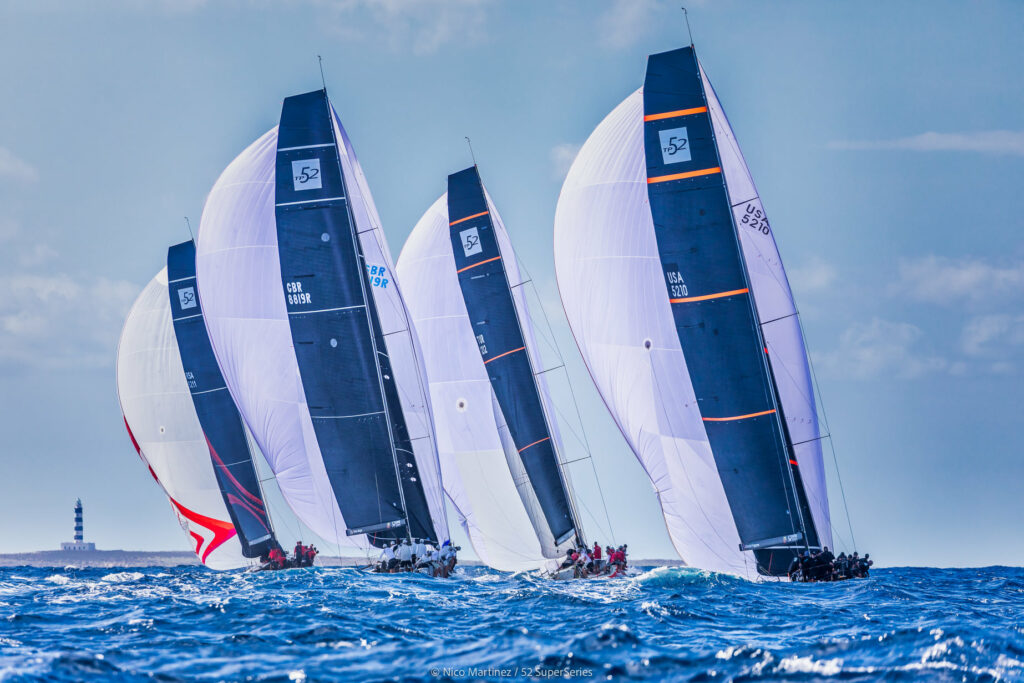 Four boats sailing downwind almost behind each other. Sailing toward land and a light house feature.