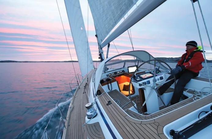 Man steering his yacht at sunset, with chart plotting devices on. 