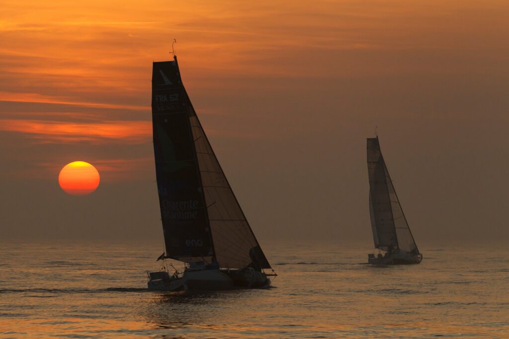 Two boats sailing during sunset on quiet waters.