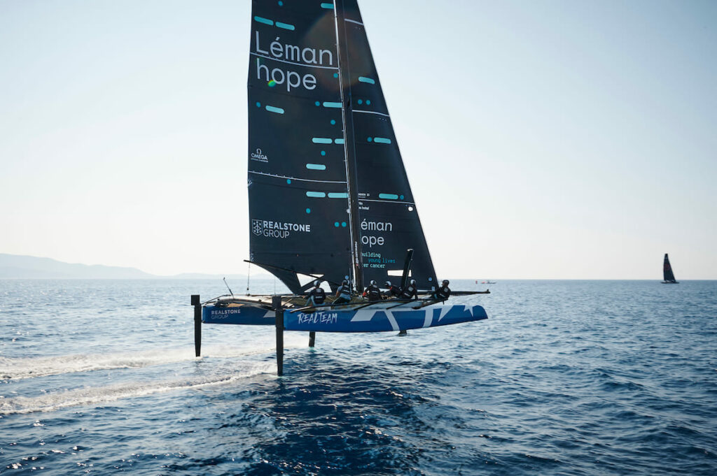 Realteam Sailing foiling, with the sun glistening on the water.