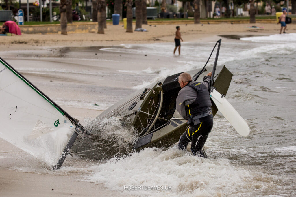 An OK dinghy being pushed by a wave onto the beach. The skipper trying to stop it from going onto the beach.