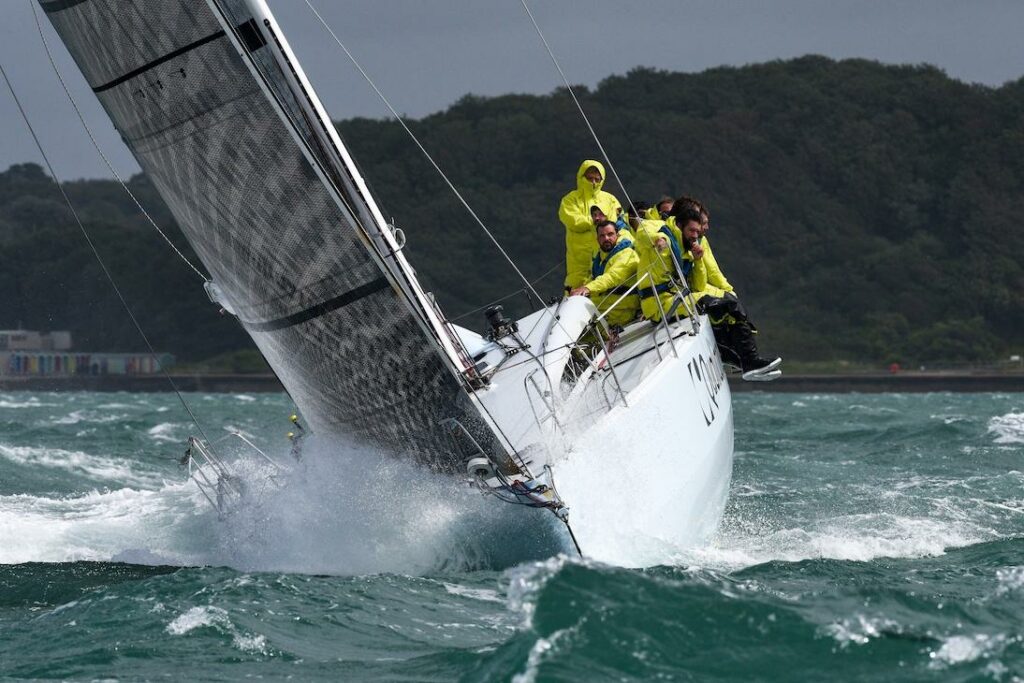 L'Ange De Milon sailing towards the camera, upwind, in plenty of chope. Crew in yellow wet weather gear leaning over the side.