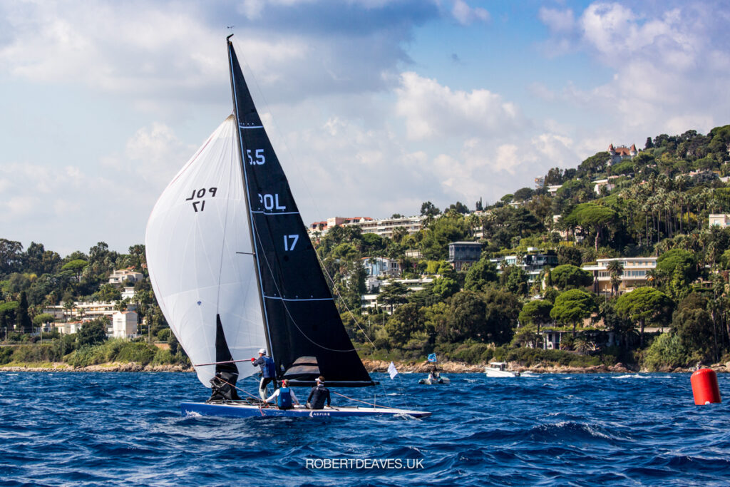 Aspire, blue hull, on a kite run. Bow person on the bow adjusting spinnaker pole.