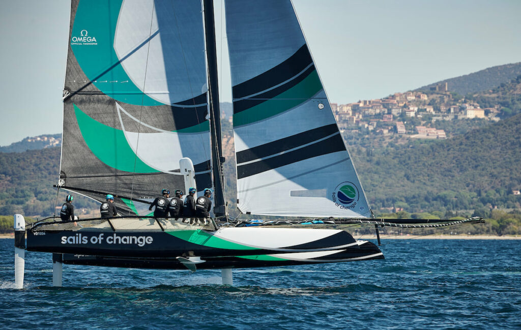 Spindrift sailing upwind on foils, crew all leaning on the wing.