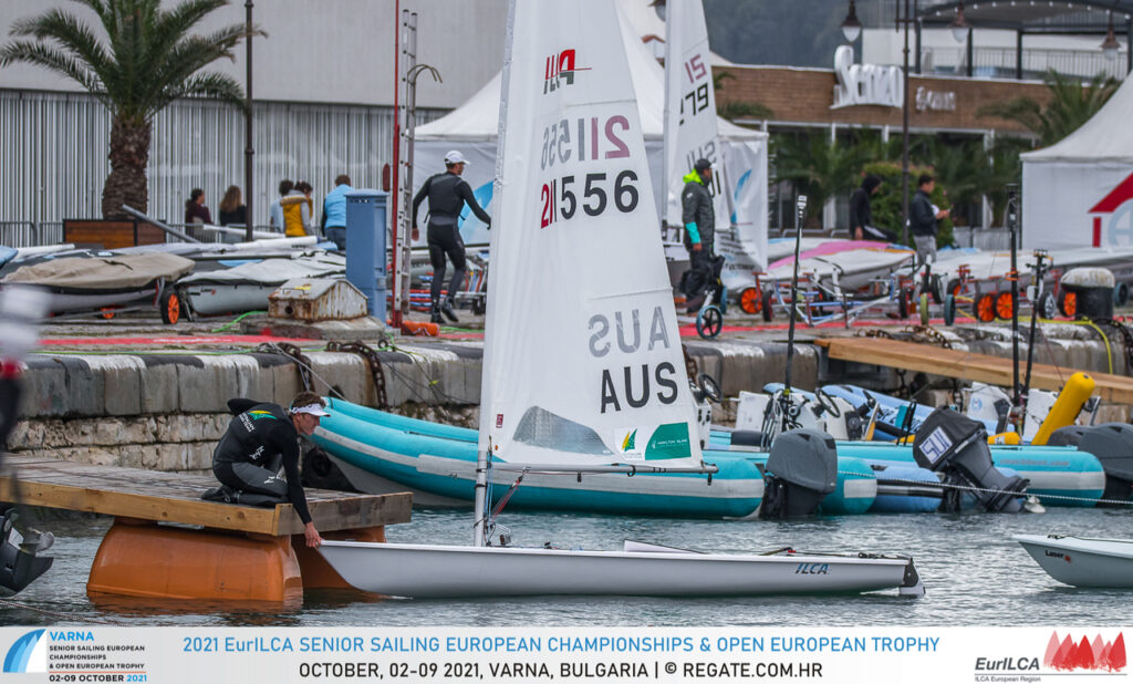 Luke Elliot on the dock, holding his laser by the bow as it sits in the water.