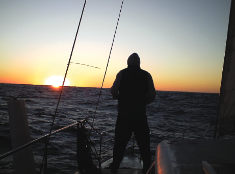 A person at the back of the sailing yacht looking onto the sunset.