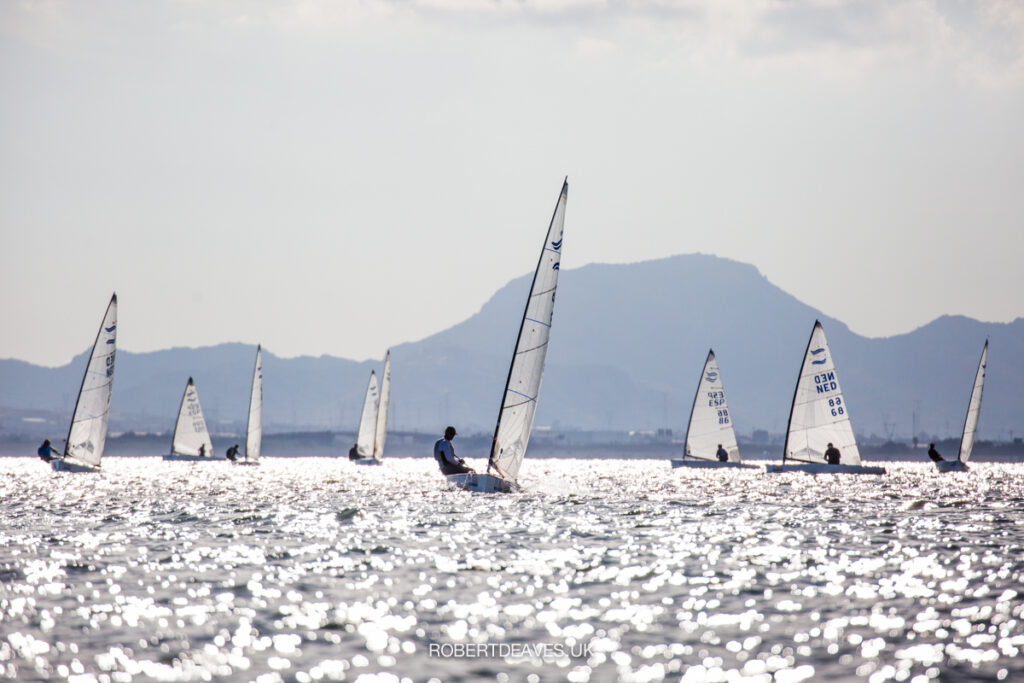 Fleet sailing upwind on different tacks. Sun reflecting on the water.