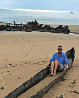 Someone sitting in a canoe like thing on a beach.