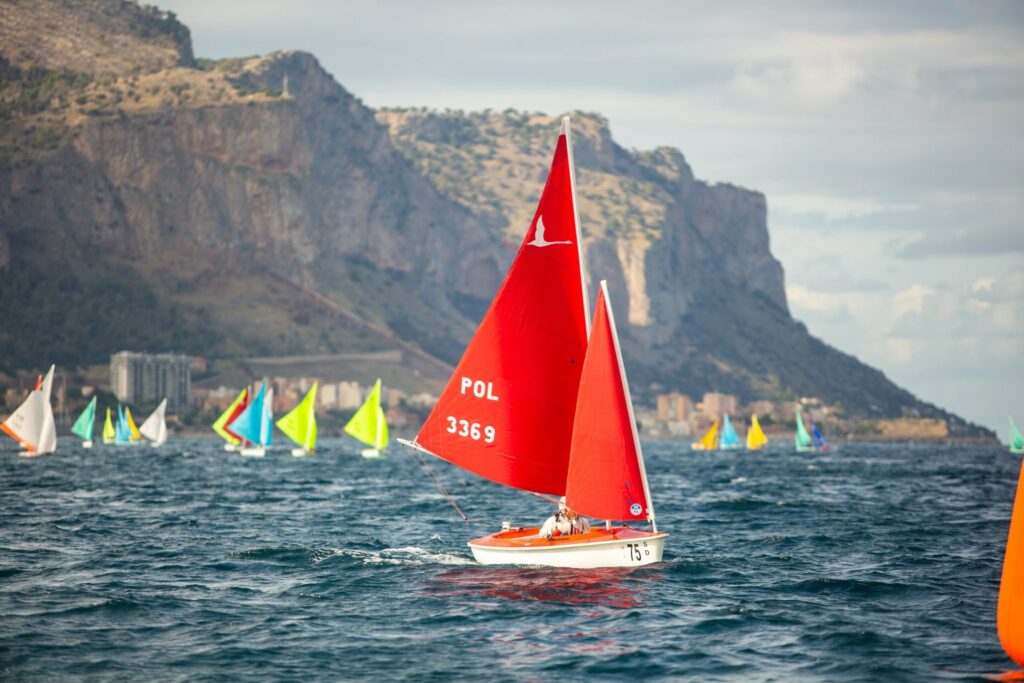 A boat from Poland sailing with the fleet and mountains behind them.