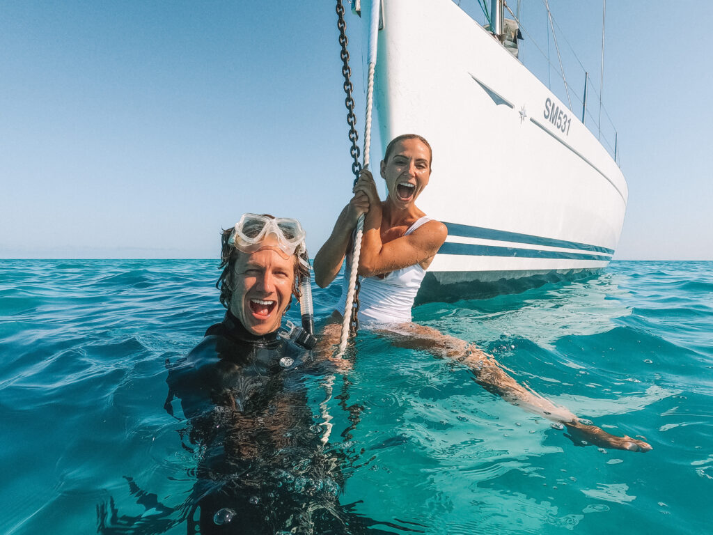 Kristina and John smiling while hanging off the anchor in the water.