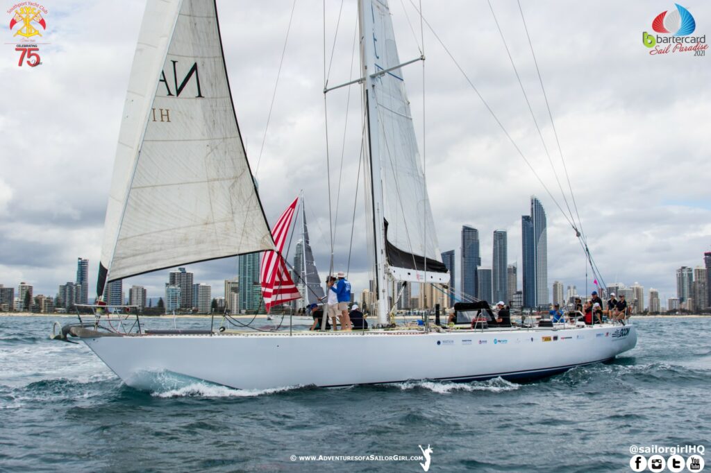 Bumblebee on a reach, a boat with s spinnaker to leeward of them, and high rises in the background.