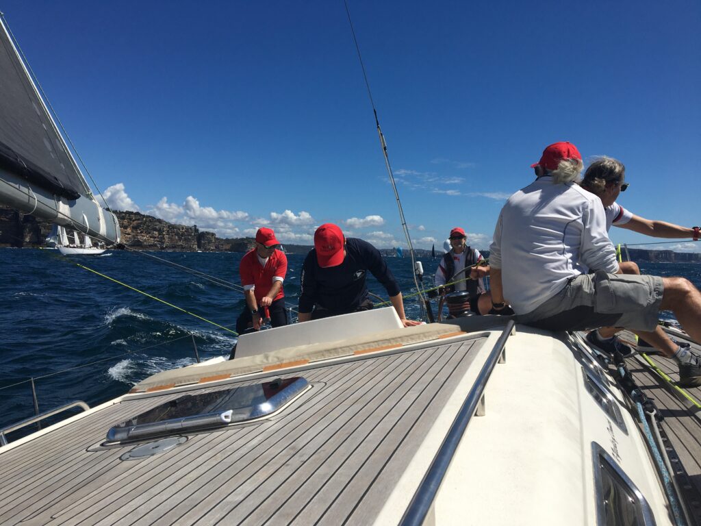 Crew working in the cockpit, skipper at the wheel, and a couple f crew on the side.