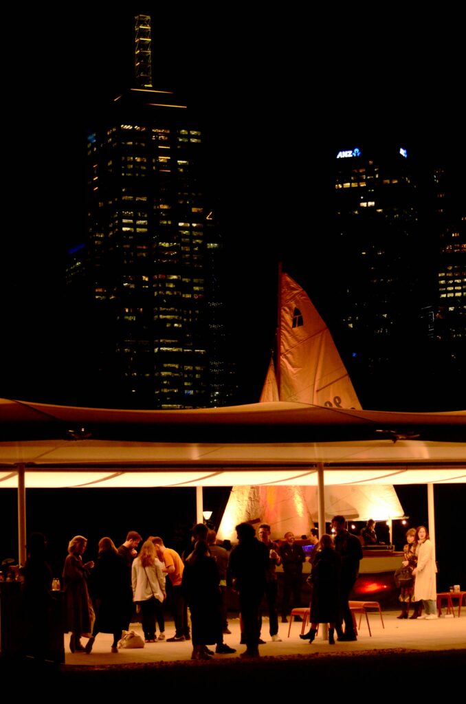 either / oar in Queen Victoria Gardens at night with the city skyline behind her.