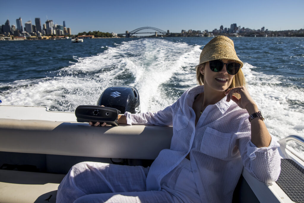 A woman holding a CS FREE at the back of a boat in Sydney harbour.