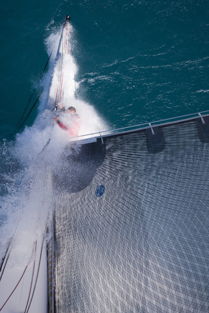 Aerial shot of bowman getting soaked, holding onto the bow sprit.