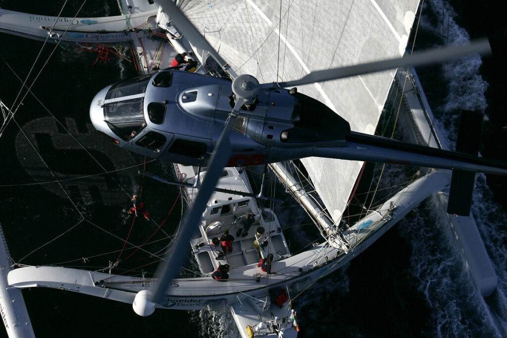 Aerial shot of a helicopter hovering over a sailing yacht.