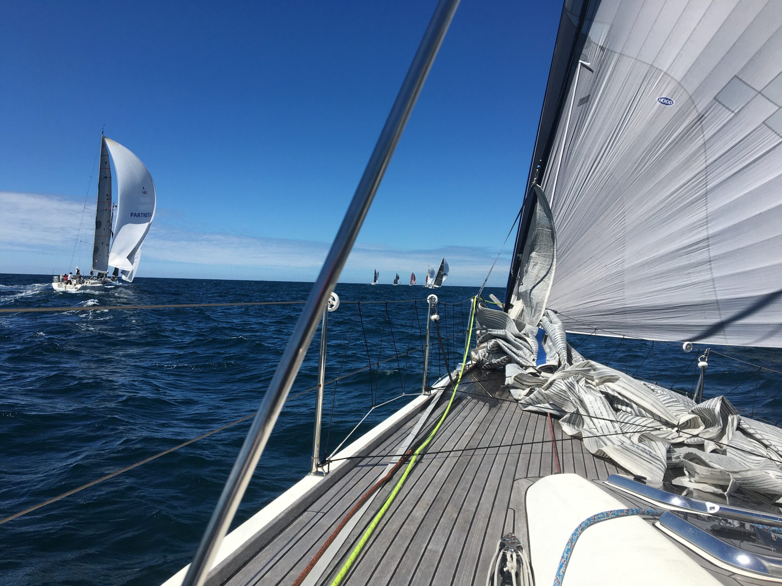 The bow of a boat with the spinnaker up, behind another boat with their kite up.