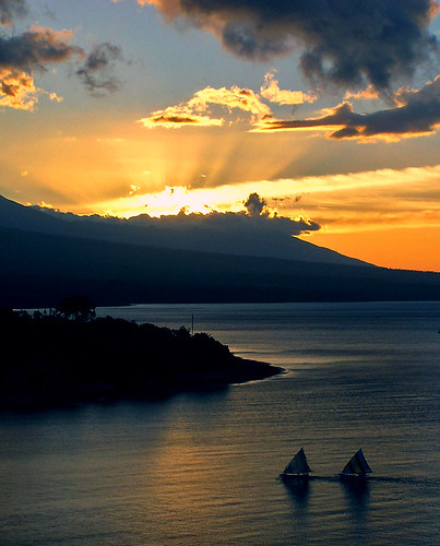 Sunset over land. Two boats sailing past a headland.