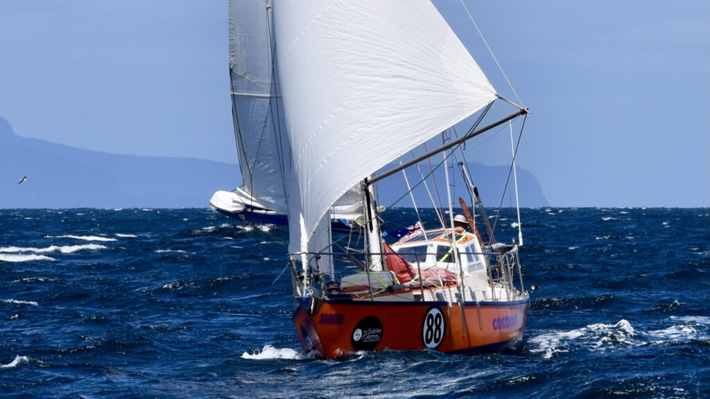 Yacht sailing downwind, headland in background.