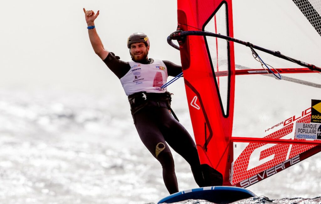 Nicolas Goyard windsurfing, hands in the air, celebrating.