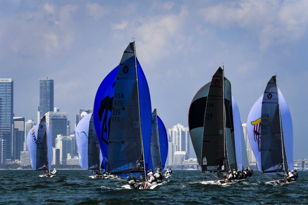 Fleet sailing on a kite reach towards city skyline.