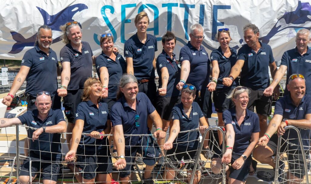 Seattle team holding out arms with something on it, smiling, on boat on dock before departure.