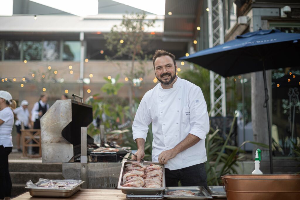 Chef holding plate of prawns next to BBQ.