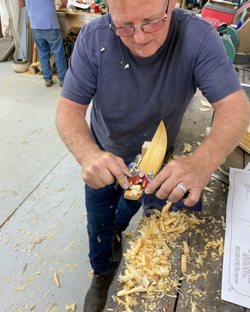 Person shaving wood from a miniature looking boat.