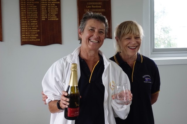 Janet Torode holding a champagne bottle and glass, with Commodore Lee Renfree.