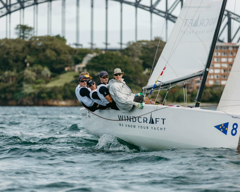 A keelboat sailing upwind with harbour bridge in background.