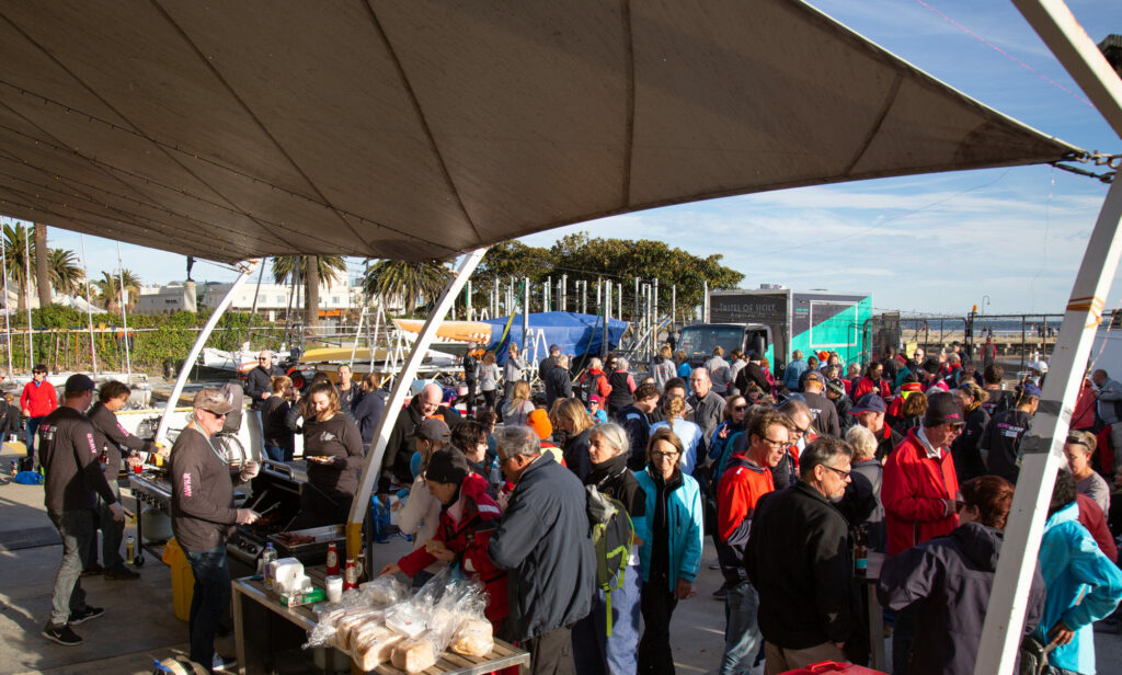 Crowd chatting outside and lining up at BBQ.