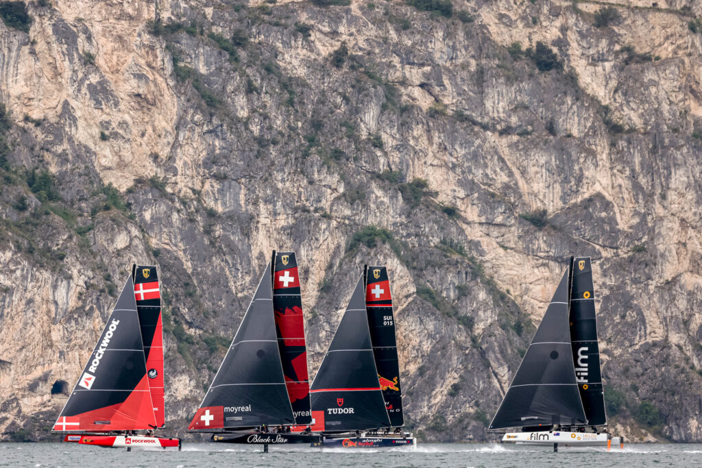 Fleet sailing upwind with cliff in background.